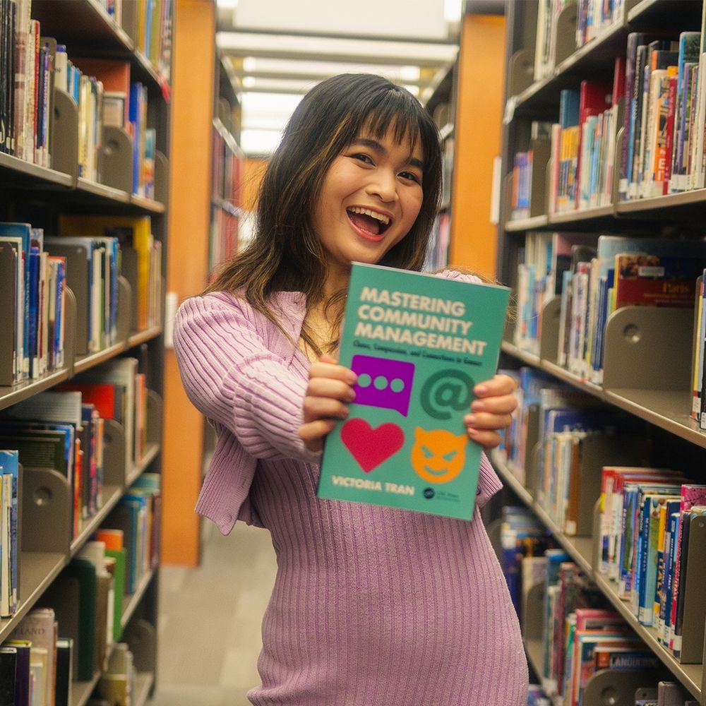 Picture of me in between shelves of books, holding up my book.