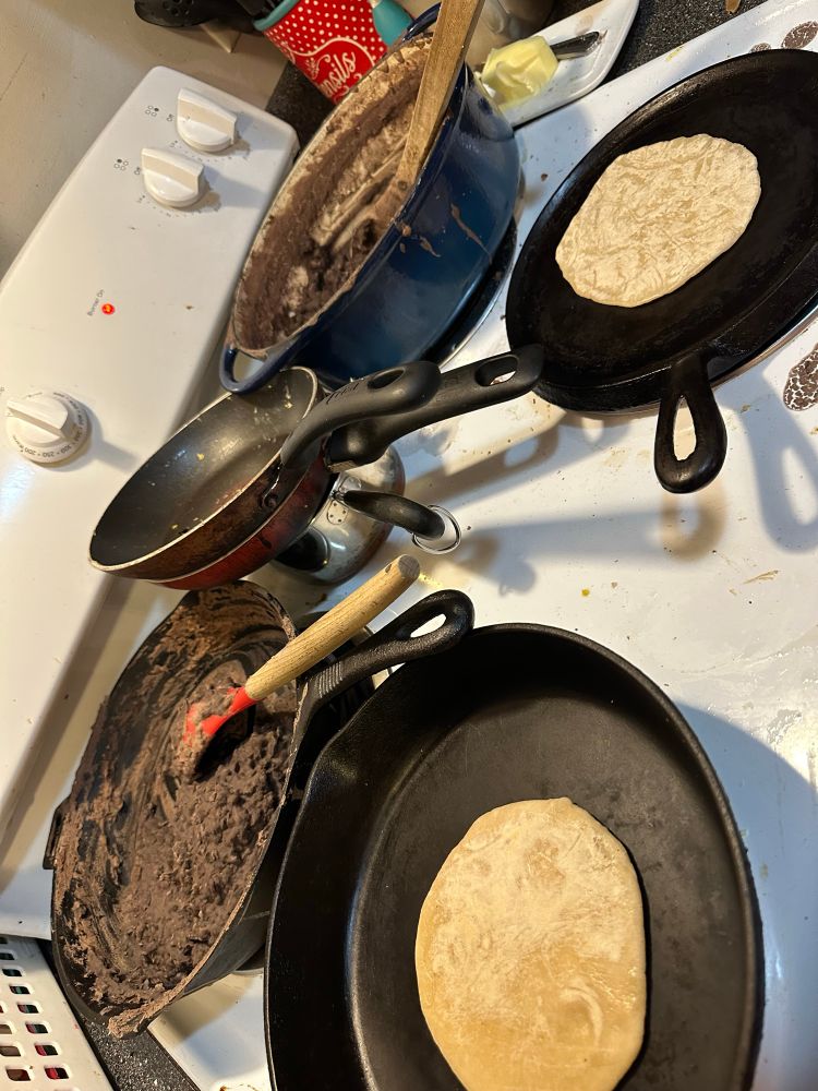 Two pans cooking tortillas, two pans cooking homemade refried black beans 