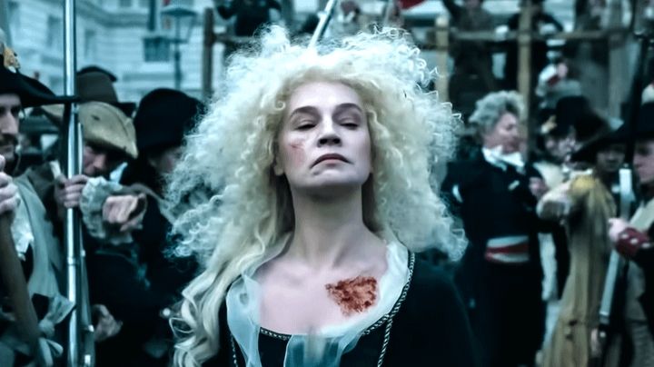 Photo of Catherine Walker as Marie Antoinette in Napoleon (2023). She is walking to her execution, dressed in black with a untidy bouffant of blonde hair.
