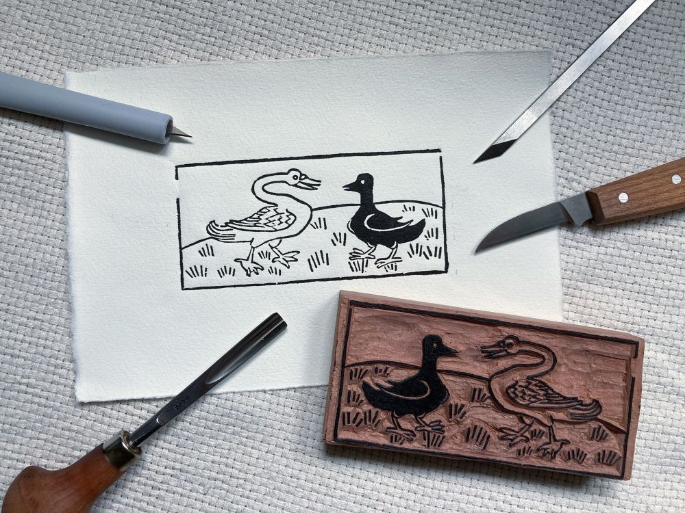 A photo featuring a woodblock and a printed impression, together with the used tools for cutting, including three kinds of knives and a gouge. 