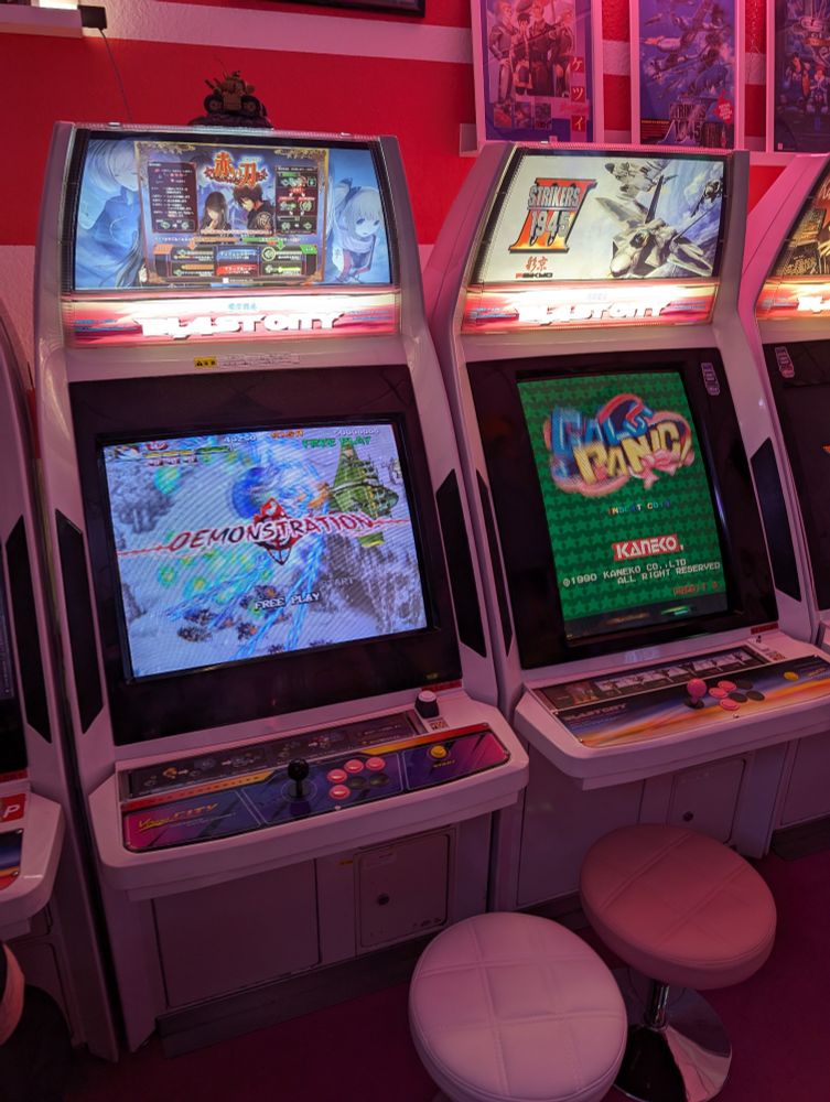 Close up on two Japanese Candy Cab arcade machines in a pink coloured room.