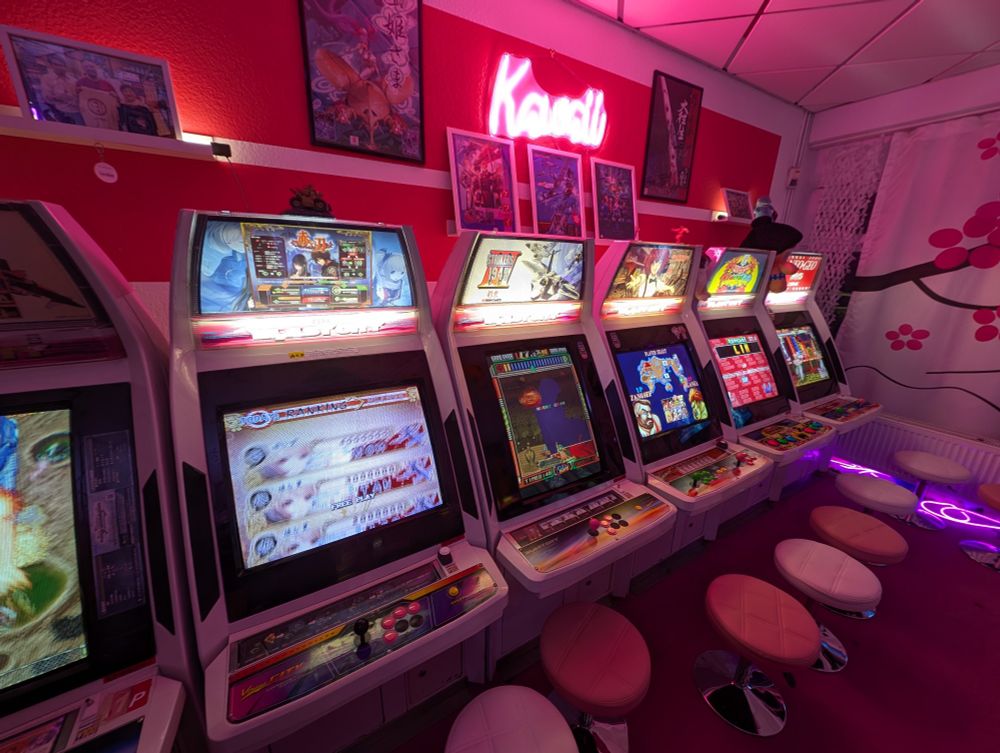 A room with a row of Japanese Arcade machines, everything decked in neon pink colours.