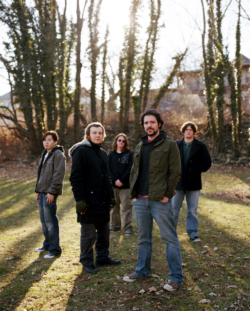 A picture of 5 men standing in a field with trees behind them.