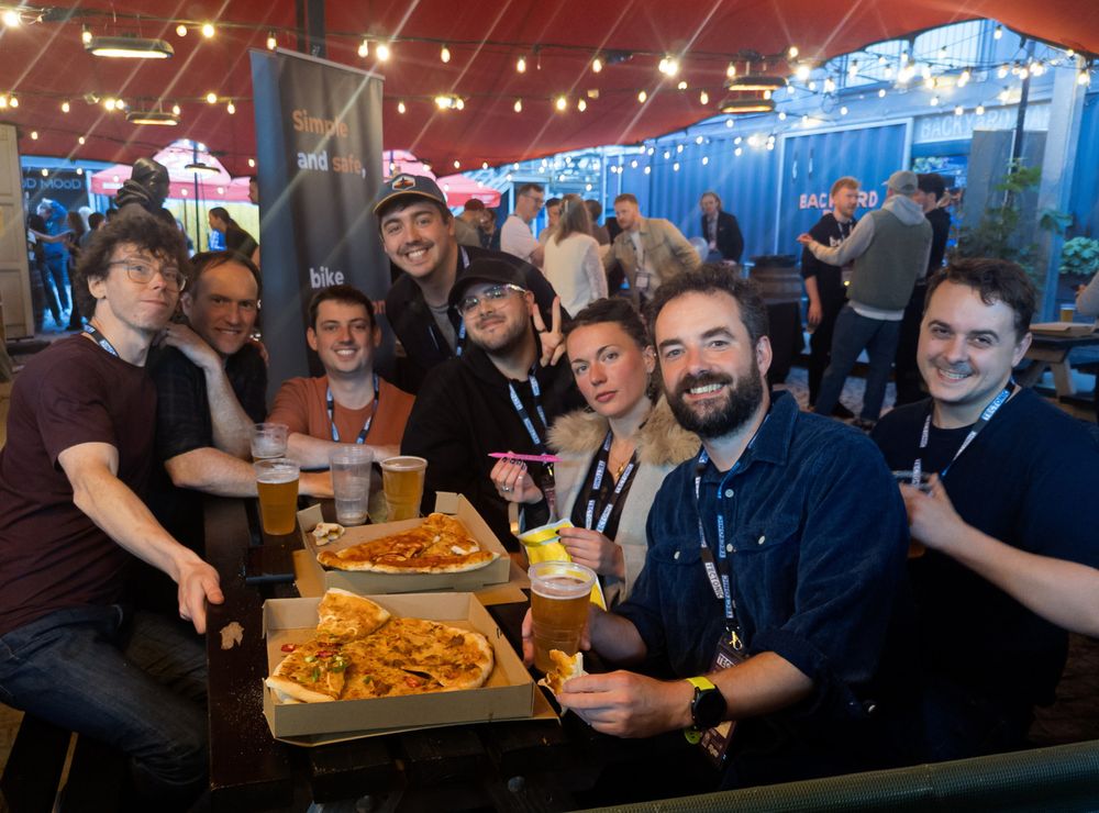 A group of people around an outdoor table with pizza and drinks