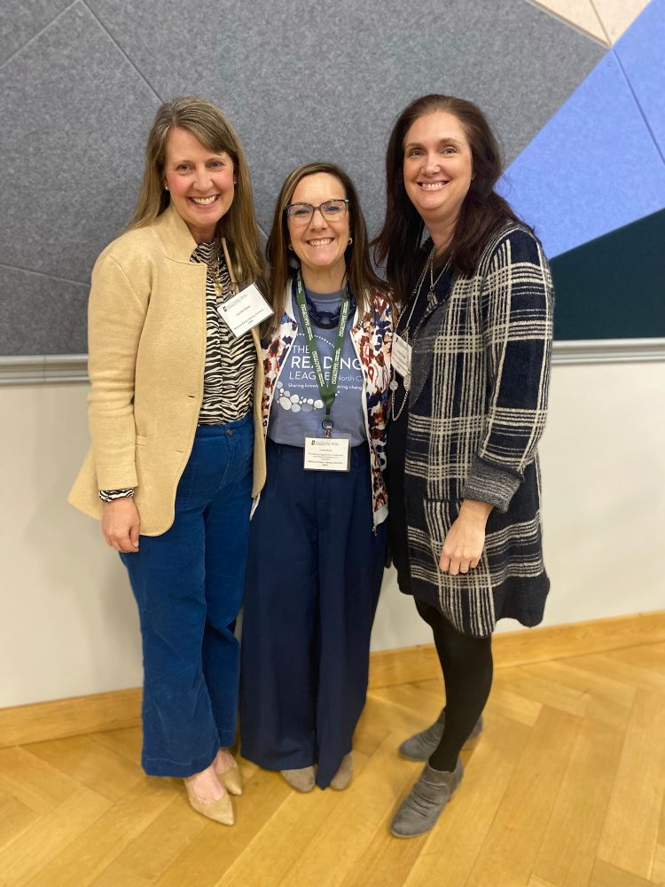 Three remain colleagues stand close together smiling. Linda stands in the center. 