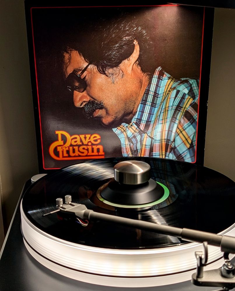Dave Grusin 'Discovered Again' vinyl LP playing on VPI Scoutmaster turntable, 12-pound acrylic platter glowing daylight white. Audio Technica AT-VM95ML cartridge.

Album cover is photo of mustachioed Grusin in a plaid shirt, in profile as he is presumably playing

Not pictured:
NAD M10v3 streaming integrated amplifier
JBL Paragon wired with Anticables

Selection from Dad's Collection
#nowplaying #nowspinning #vinyl #sheffieldlab #audiophile