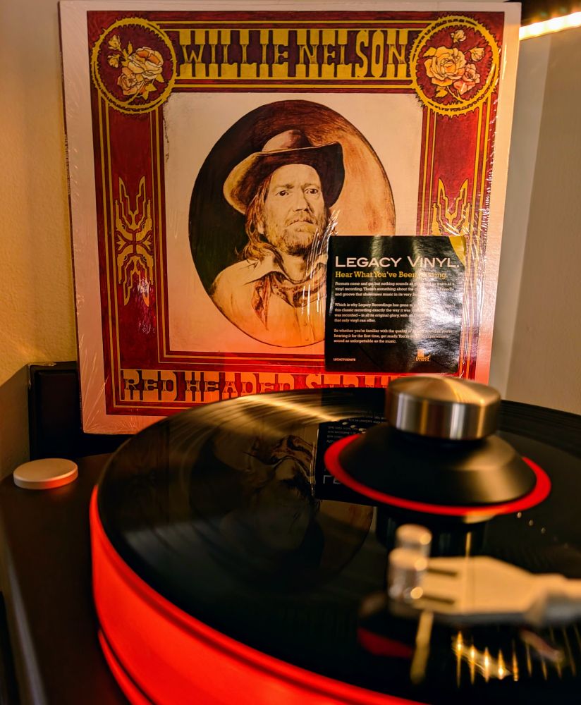 Selection from Dad's Collection #72
Willie Nelson - Red Headed Stranger, Columbia Legacy Vinyl reissue
Playing on VPI Scoutmaster turntable, 12-pound acrylic platter glowing red. Audio Technica AT-VM95ML cartridge.

Cover:
Main image: A sepia-toned, almost Old West–style framed portrait of Willie Nelson, shown in a circular vignette. He’s wearing a cowboy hat and long hair, looking like a weathered outlaw figure — exactly in line with the concept of the album.

Design: The portrait is set inside an ornate gold and red border that resembles an antique wanted poster or an old saloon painting frame.

Text: At the top, in bold western-style lettering, it reads “WILLIE NELSON”; at the bottom, “RED HEADED STRANGER.”

Feel: The whole presentation is rustic, sparse, and haunting, matching the stripped-down sound of the record.