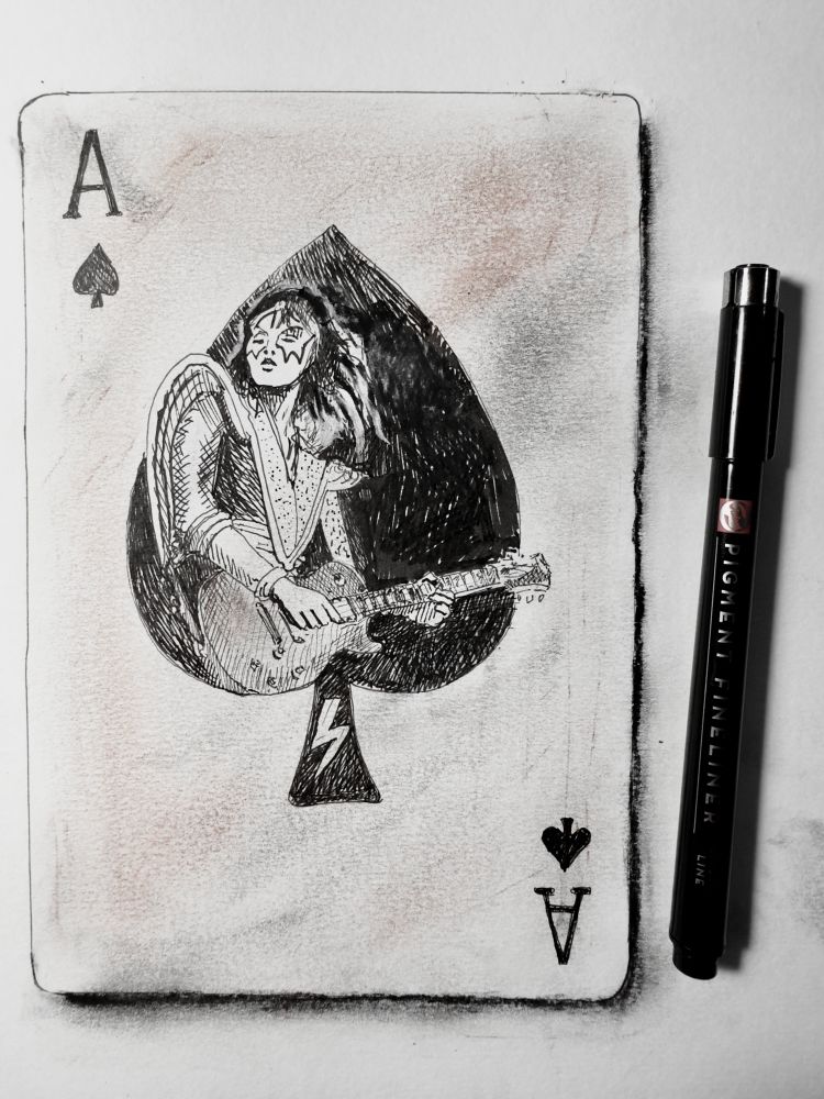 Ace of spades card design with a drawing of Ace Frehley in the centre. A pen sits on the page, to the right