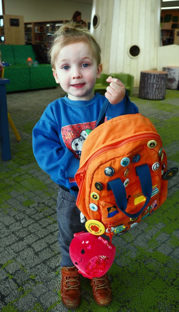 Kid holding a backpack with buttons at the Forest Park Branch Library.