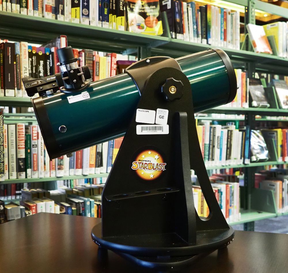 Small telescope on a table with books in the background.