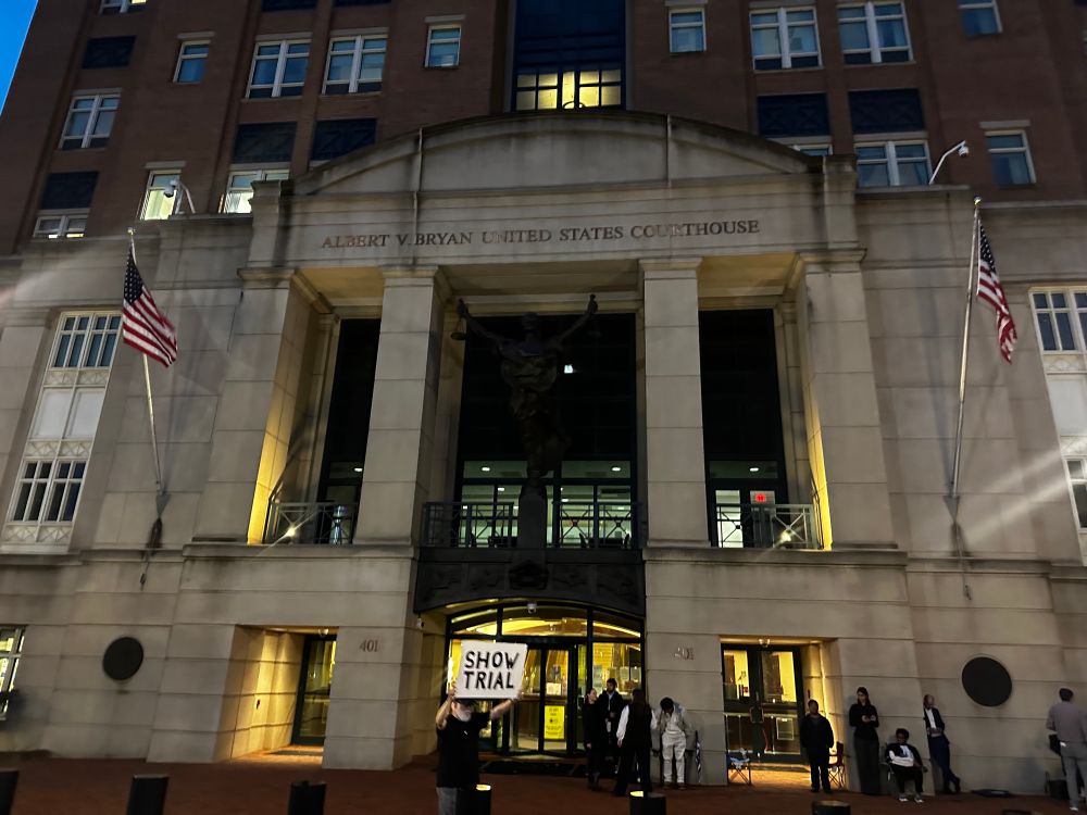 Federal courthouse in EDVA, with line of people out front and a guy holding a “show trial” sign 