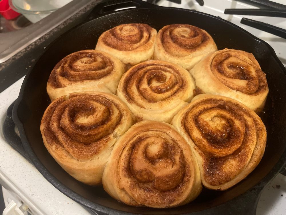 An iron skillet containing eight freshly-baked cinnamon rolls, moments after being pulled from the oven. They smell heavenly.