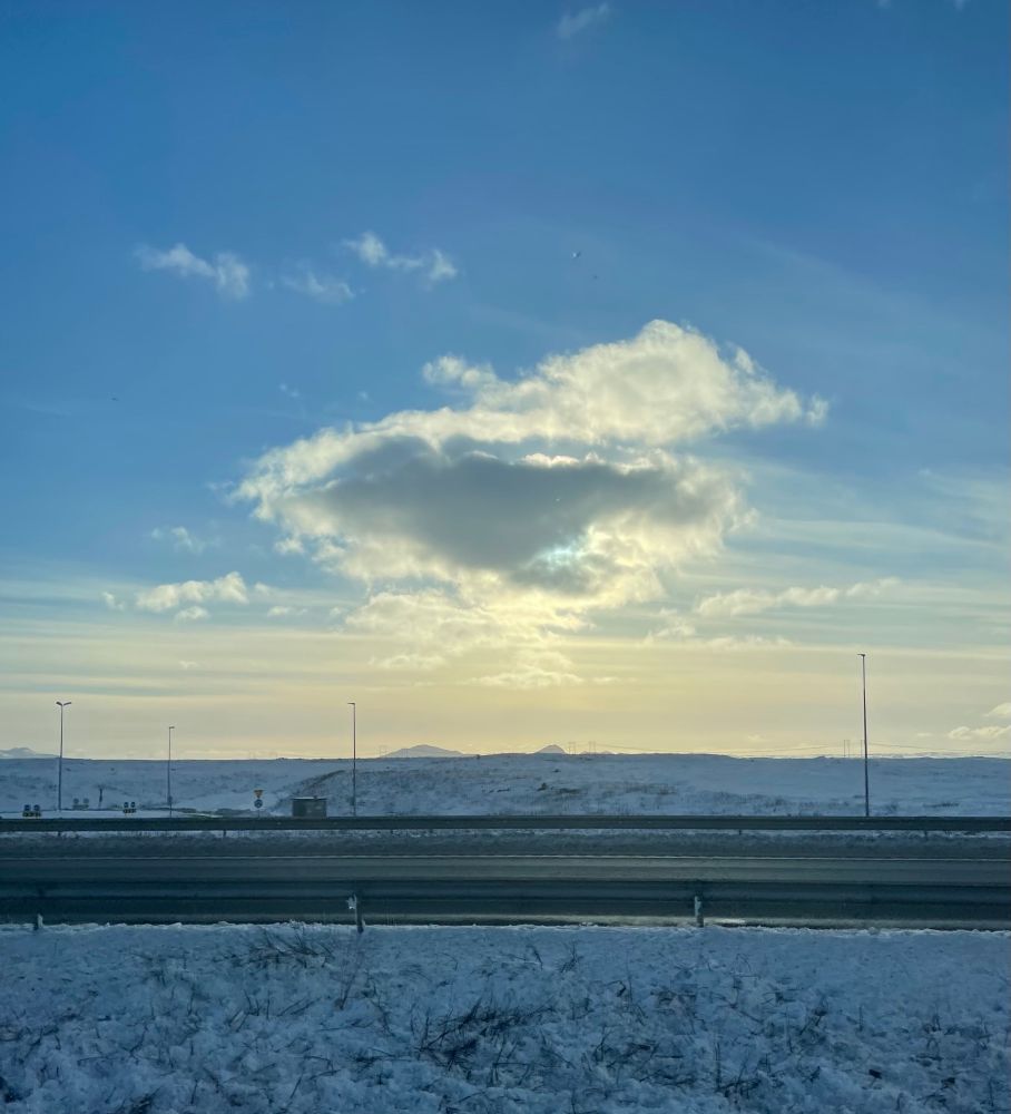 Sun behind a cloud over snowfields along the road, Iceland, daytime.