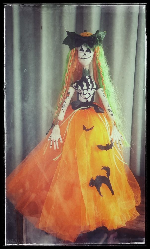Photo of a doll stading in front of a curtain, with a big orange skirt.