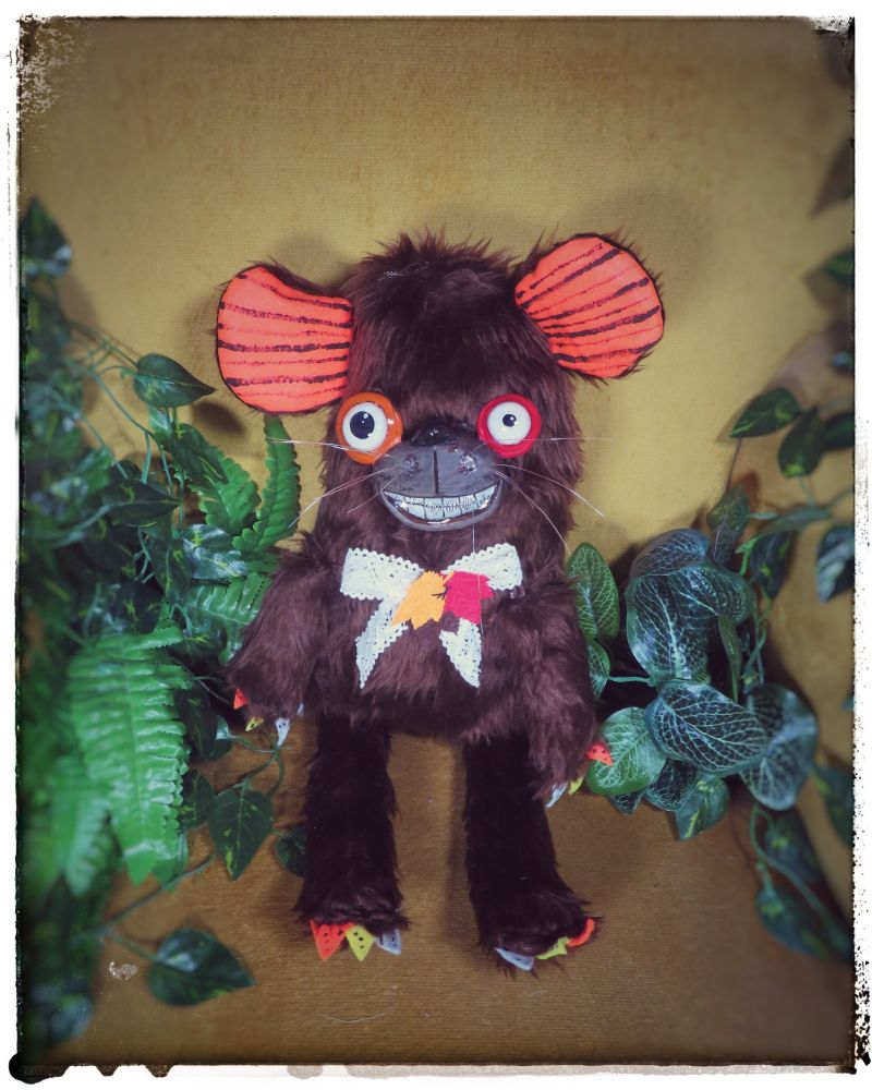 Photo of a bear plush sitting on a yellow chair with faux greenery around him.