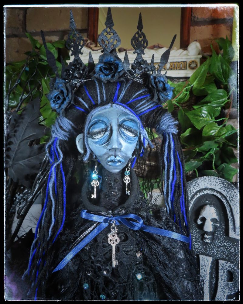 A close up of a ghost doll that sits amongst a grave and various faux flora.