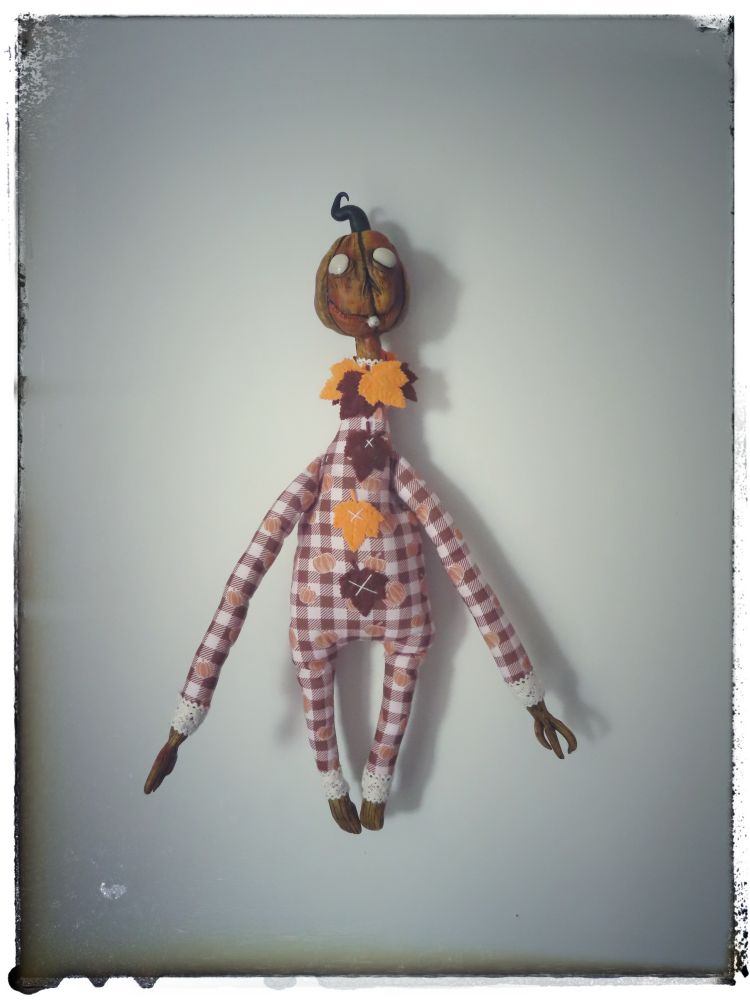 White wall, with a pumpkin headed doll hanging on it.