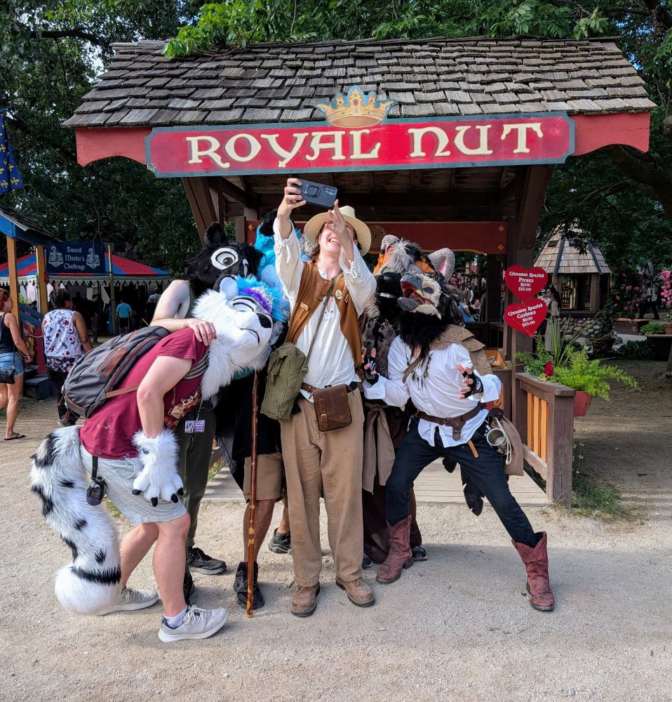 Group of furries taking a selfie with a Renaissance Faire attendee in front of the Royal Nut stand