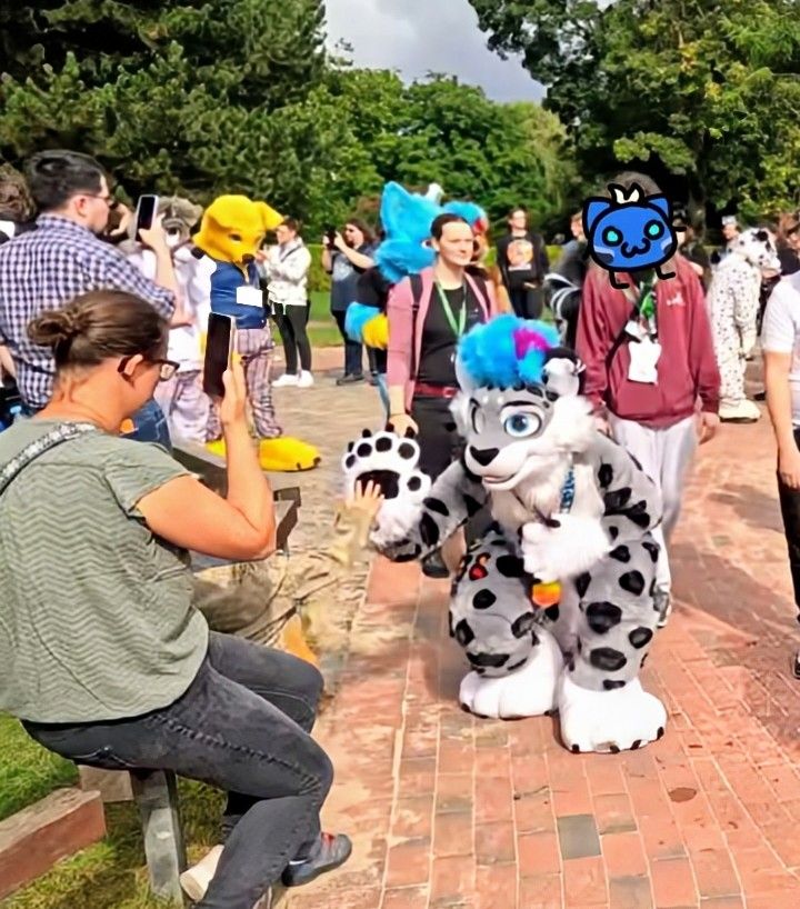 Silver, in fullsuit, giving a high five to a small child during the fursuit parade through the park