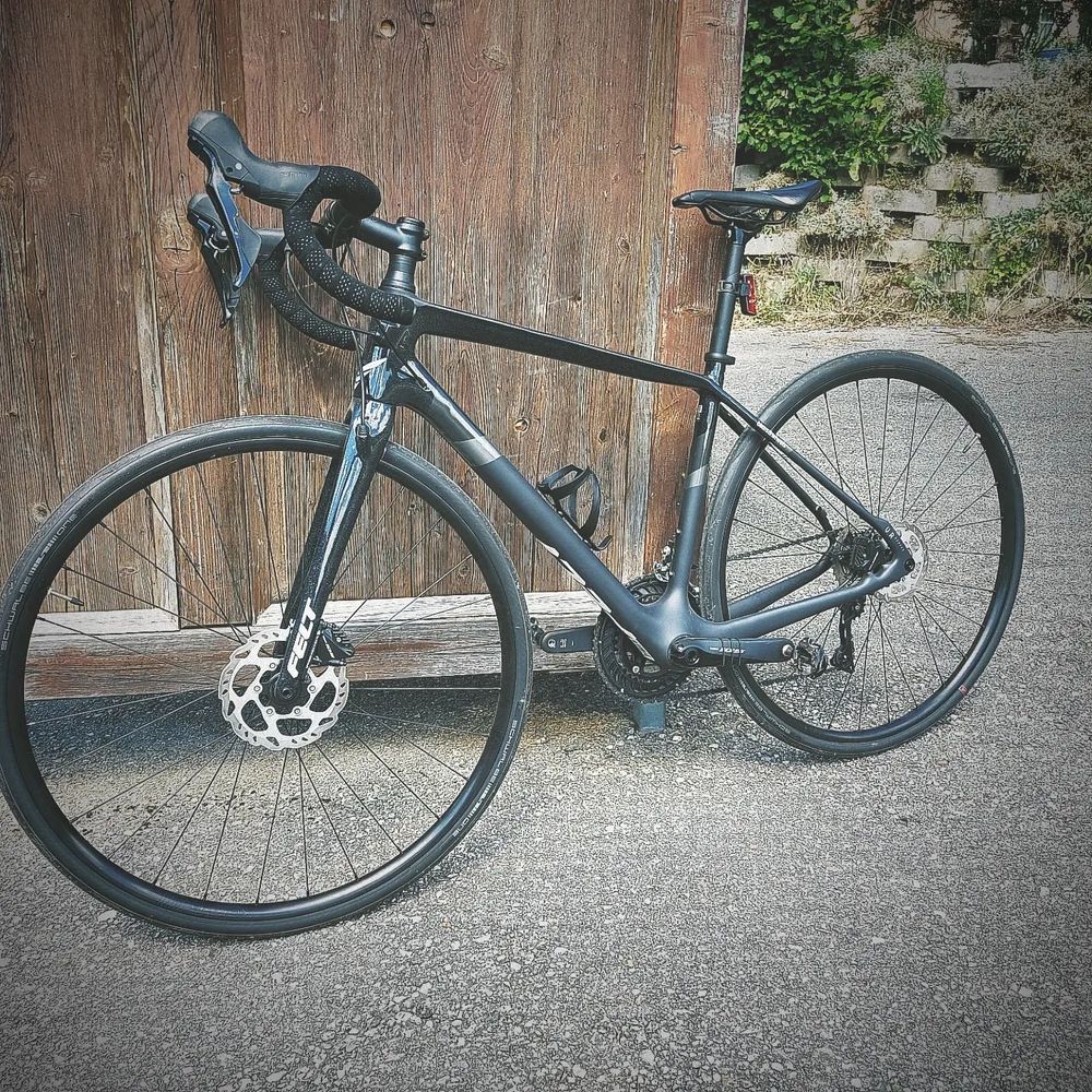 Schwarzes Rennrad außen an die Seitenwand eines hölzernen Bushäuschens gelehnt