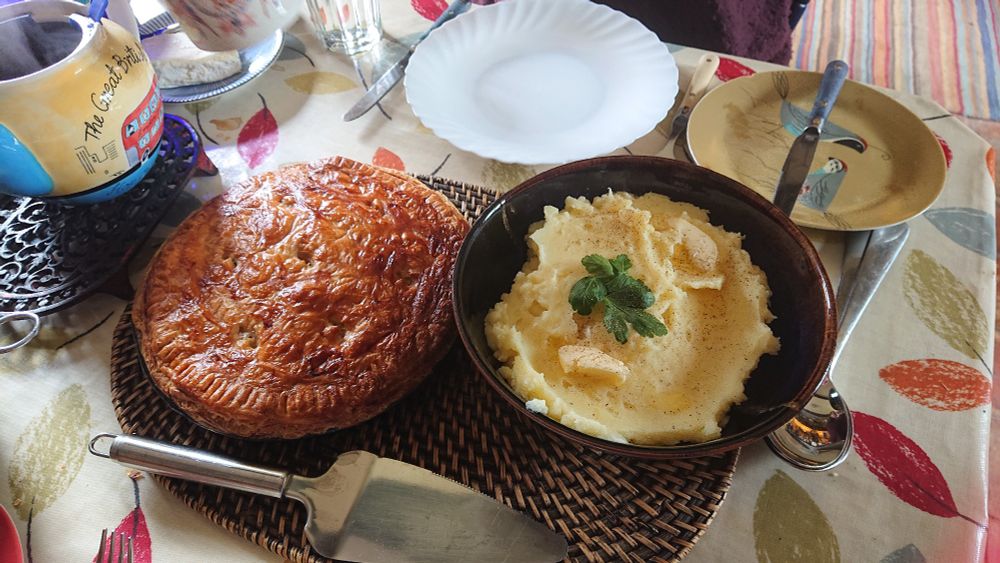 A golden crusted pie next to a bowl of mashed potato. 