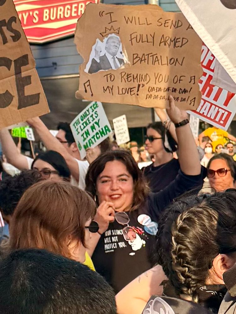 Former assemblywoman Wendy Carrillo at a protest carrying a sign that says I will send a fully armed battalion to remind you of my love, with a picture of Trump making a face