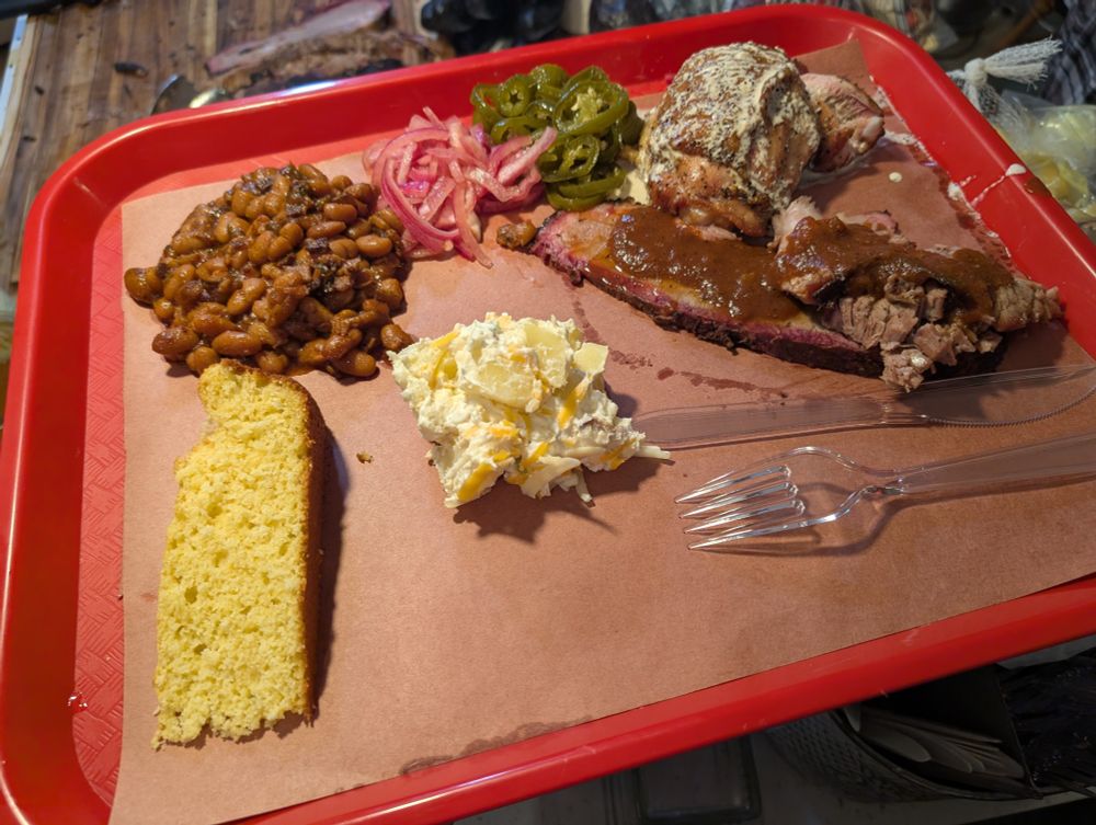 A cafeteria tray loaded with homemade smoked brisket, barbecued chicken, cornbread, and various other side dishes.
