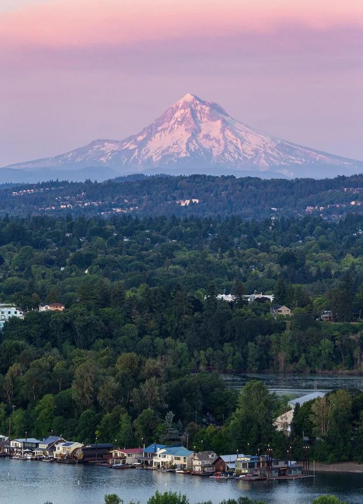 A beautiful sunset view of the Columbia River at Portland, Oregon. Houseboats float along the shore in the foreground, while Mt. Hood glows in the light of the setting sun in the distance. 
