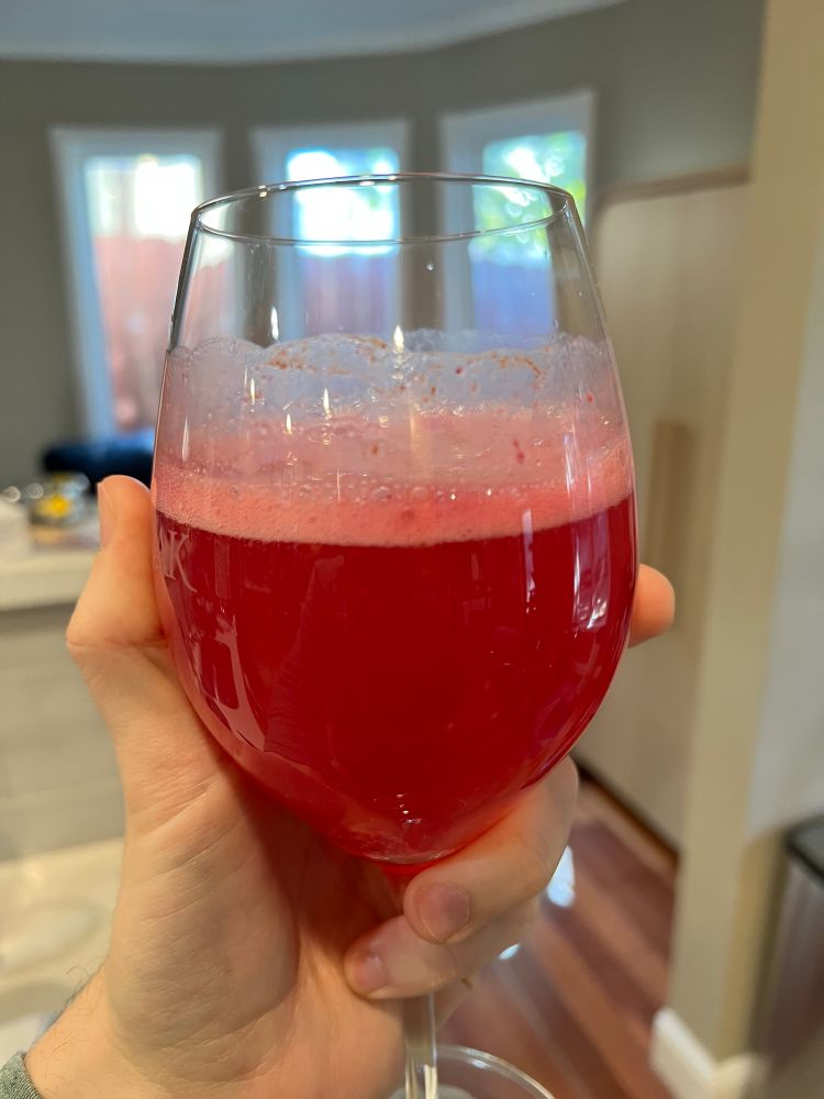 Wine glass filled with red liquid and foamy bubbles sitting on top of the liquid.