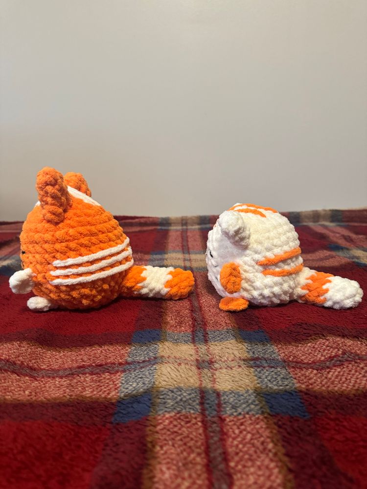 Two crocheted kittens (one orange with white accents, and the other white with orange accents) pictured from the side