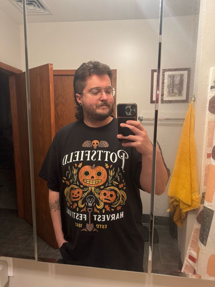 Just a guy wearing a black T-shirt with pumpkins from “Over the Garden Wall”. The shirt has text that reads ‘Pottsfield Harvest Festival ESTD 1502’ 