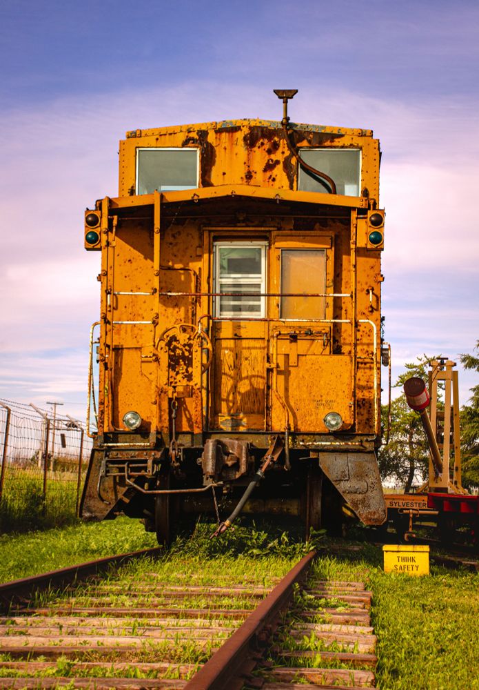 An old orange rail car that is now used for display in an outdoor train museum. 