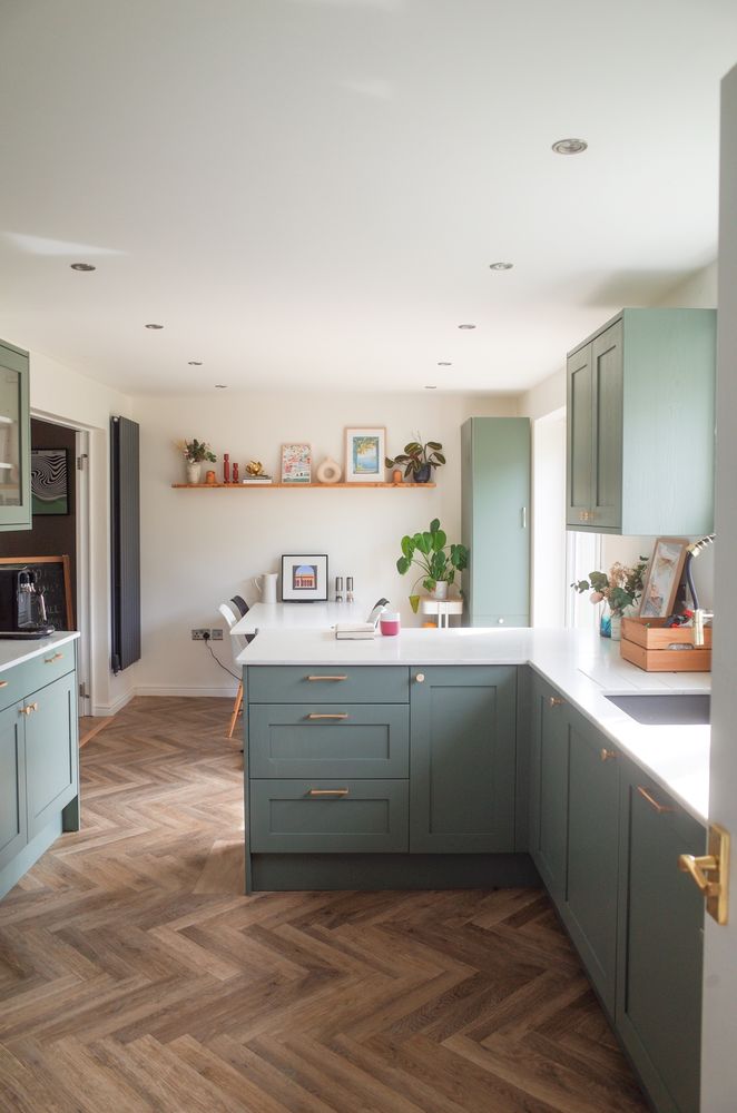 newly renovated kitchen with green cabinets, carrara quarts countertops, herringbone flooring, and minimalist decor.

