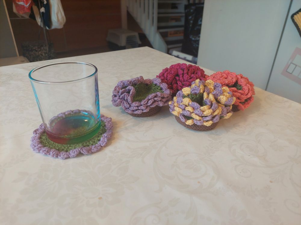 Home
Notifications
Explore
Live feeds
Private mentions
Bookmarks
Favorites
Lists
Preferences
Alt text

Four sets of crochet coaster. Each set contains four coasters with a green center and an edge that looks like flower petals in various colors (purple, pink, yellow). Each coaster set is bunched together and placed in a brown crochet basket. This makes the set look like a colorful potted plant. One coaster is placed next to the sets and a glass has be put on top of it.