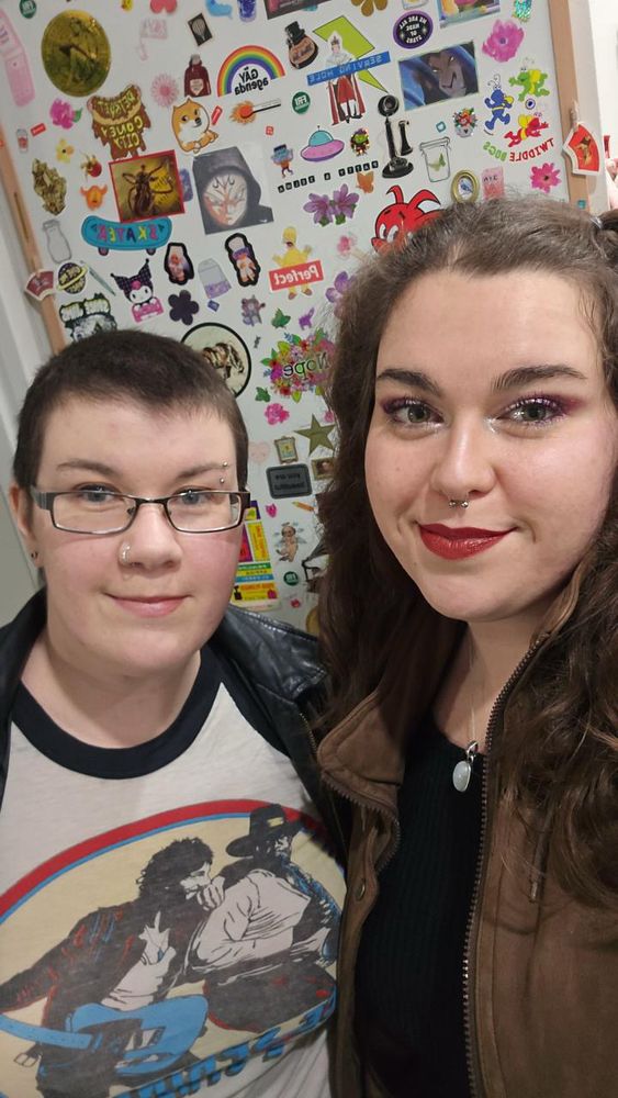 Two young white women, one with short dark hair and glasses, one with long brown curly hair 
