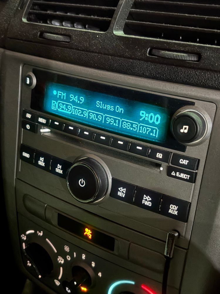 A car radio dial shows “slugs on” as the title of song/artist

