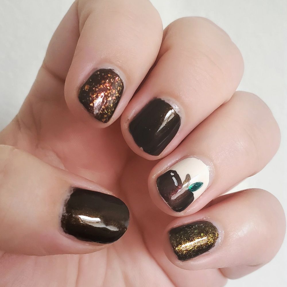 A white lady's hand with a fall themed manicure, featuring nail polish in shades of a dark brown shimmer, oxblood red with red orange and gold metallic flakes on top, a dark brown with bronze yellow flakes, and a sparkly red apple with green leaf on an off white background.