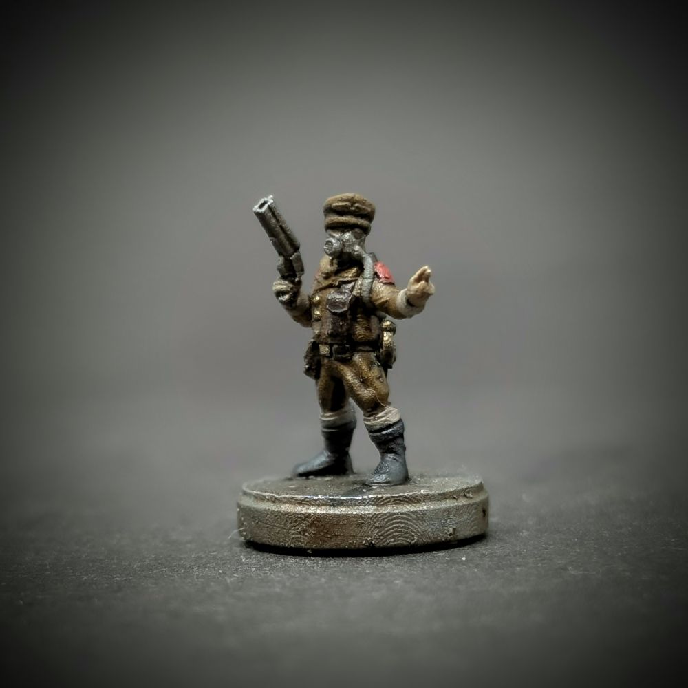 A tiny 3d printed model of an airship pilot. He wears a brown, early twentieth century style jumpsuit, a peaked cap, and a rebreather. On one hand he carries a pistol.