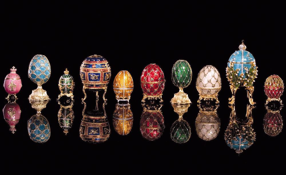 Eine Reihe kunstvoll verzierter Fabergé-Eier steht auf spiegelndem schwarzen Untergrund.

