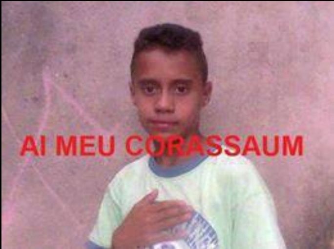 Menino de uniforme escolar com a mão no peito, na frente está escrito AI MEU CORASSAUM