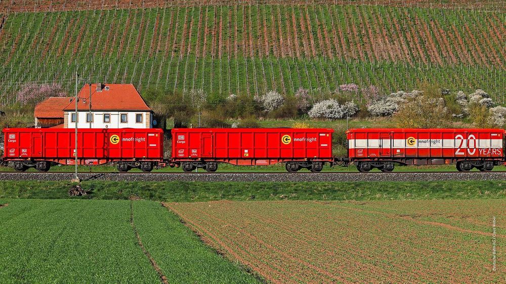 Ein Güterzug fährt vor einem Weingut vorbei, durch die Perspektive sitzt das Gutshaus direkt auf einem Güterwagen.