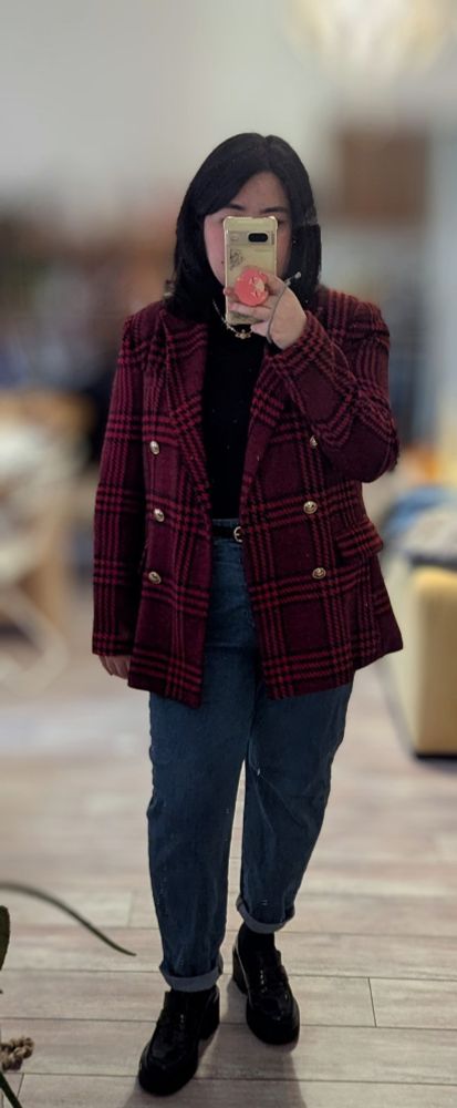 Mirror selfie of a woman wearing an open red checkered double breasted jacket with golden buttons, a black turtleneck, high waisted mom blue jeans, a thin black belt, black loafers and a pearl necklace.