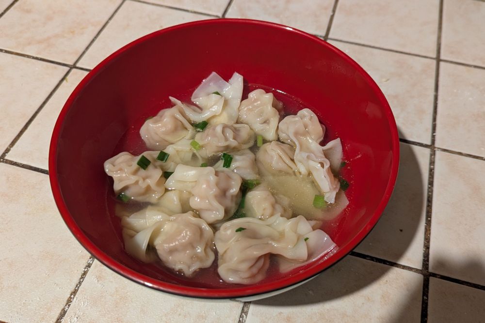 A bowl of wonton in soup placed on a tiled counter