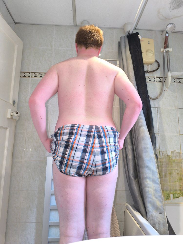 Full body image of a white, masc presenting person with short ginger hair wearing nothing but boxers, from the back