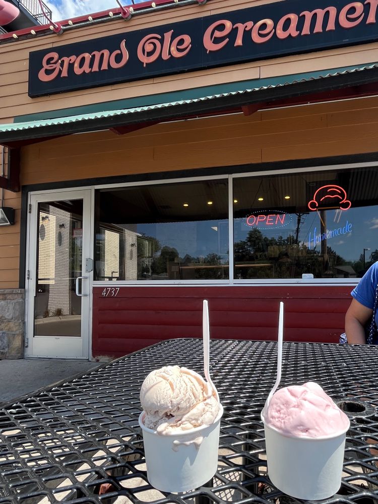 Two cups full of ice cream in front of a small storefront.