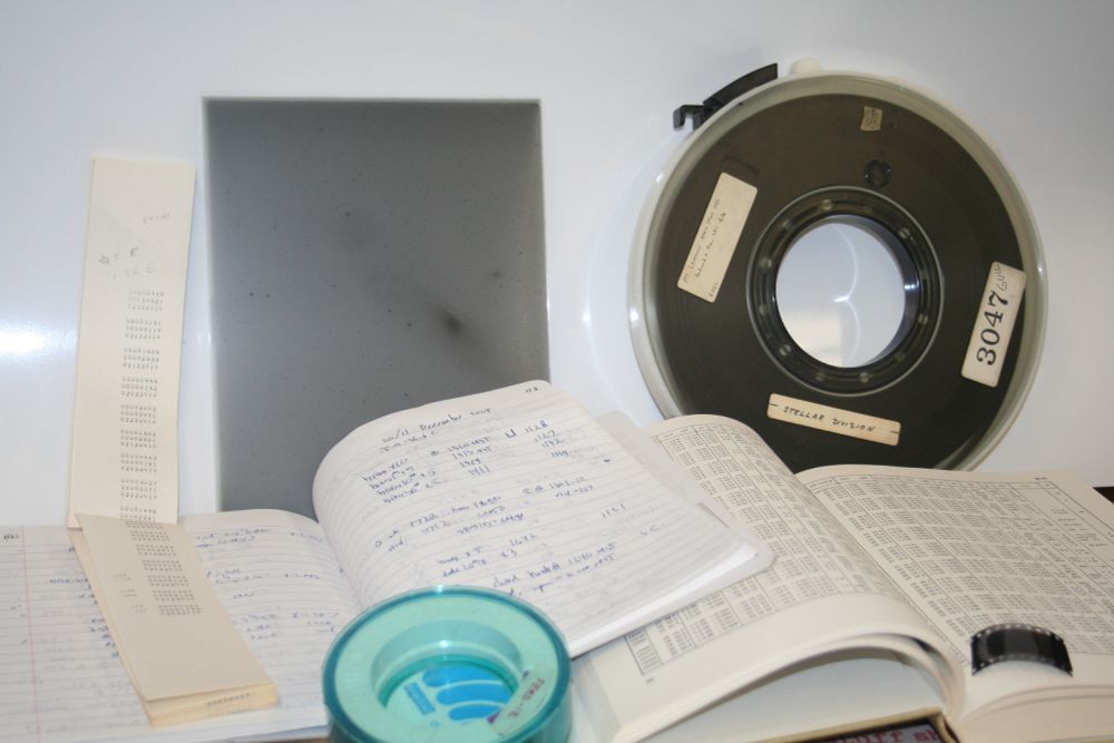 Astronomical data over the decades: in printed tables, handwritten logbooks, grocery-tape numbers, photographic plates, DEC TK-50 and 9-track tape reels, and 35mm film frames.