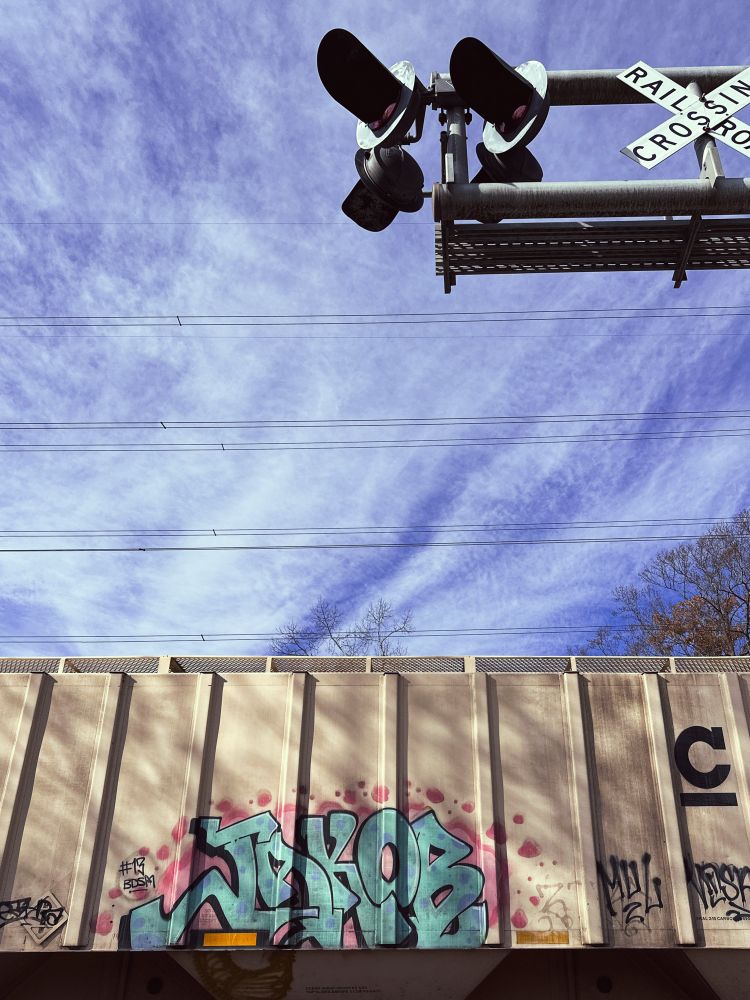 A passing freight train car with graffiti against a partly cloudy sky