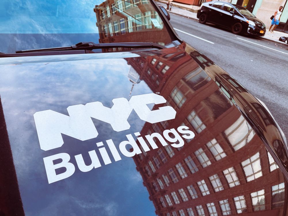 Buildings reflected on the hood of a black vehicle with the logo NYC buildings 