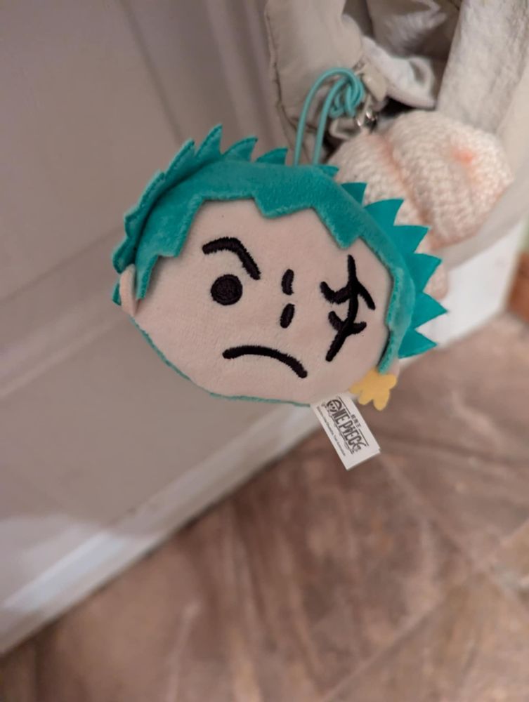 Bag charm of Roronoa Zoro. He is just a head in a cartoonish style with green hair and a scar on his right eye. 