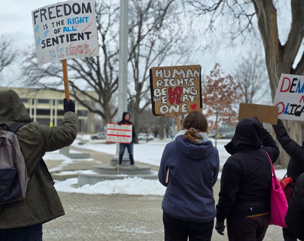 Backs of protestor. Sign on the left: freedom is the right of all sentient beings. Sign on the right: human rights belong to everyone 
The Lo of belong and the ve of everyone are in red to show the word love